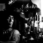 man wearing hat beside bottles on grayscale photography