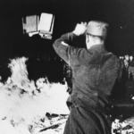 A member of the SA throws confiscated books into the bonfire during the public burning of "un-German" books on the Opernplatz in Berlin.