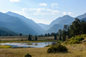 a grassy field with a lake and mountains in the background